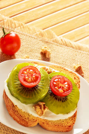 Toast with kiwi, cheese and cherry tomato on a piece of sackcloth in wooden board.の写真素材