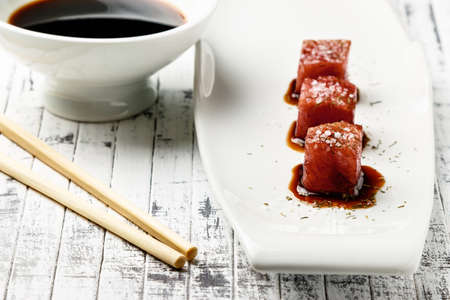 Tuna sashimi dipped in soy sauce,  thick salt and dill on old white wooden board with chopsticks and sauce bowl. Raw fish in traditional Japanese style. Horizontal image.の写真素材