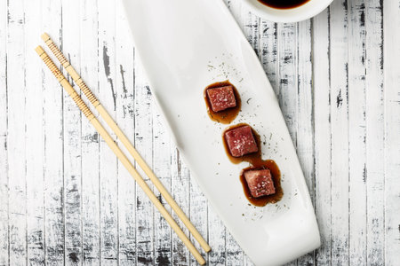 Tuna sashimi dipped in soy sauce,  thick salt and dill on old white wooden board with chopsticks and...