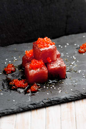 Tuna sashimi dipped in soy sauce with salmon roe, thick salt and dill on slate stone. Raw fish in traditional Japanese style. Vertical image.の写真素材