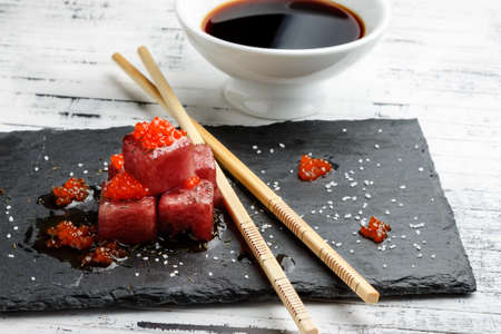 Tuna sashimi dipped in soy sauce with salmon roe, thick salt and dill on slate stone with chopsticks and bowl with soy. Raw fish in traditional Japanese style. Horizontal image.の写真素材