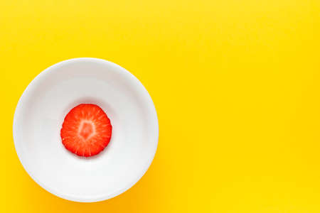 Slice of fresh strawberry on a round white plate on yellow background. Horizontal image seen from above.の写真素材