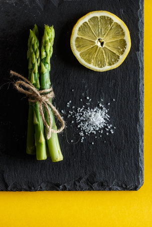Asparagus. Bunch of fresh green asparagus with coarse salt and a slice of lemon on a slate plate on...