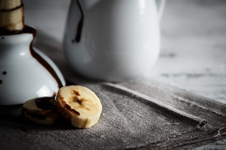 Delicious dessert of fresh banana slices with chocolate on top on a sackcloth seen from close up. Horizontal image of dark moody style.の写真素材