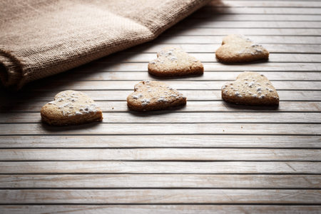 Delicious heart-shaped homemade cookies sprinkled with icing sugar on a wooden board with sackcloth...