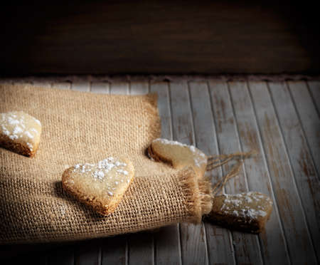 Delicious home-made heart-shaped cookies sprinkled with icing sugar on sackcloth and wooden boards. Horizontal image.の写真素材