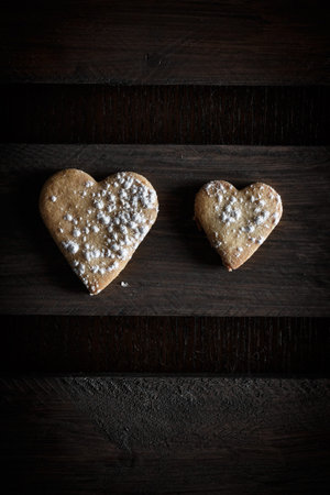 Two delicious home-made heart-shaped cookies sprinkled with icing sugar in a wooden board. Vertical...