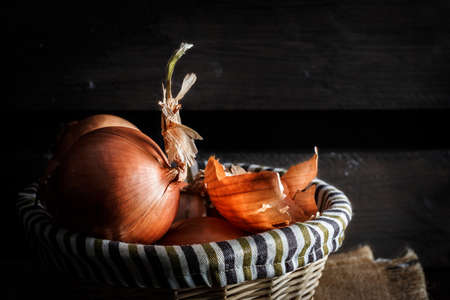 Onions in a wicker basket with wooden boards in the background. Rustic style. Horizontal image.の写真素材