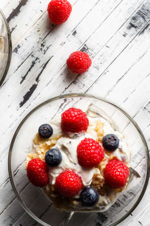 Raspberries, blueberries, cereals and yogurt in a glass bowl on wooden slats. Healthy breakfast for a healthy life. Vertical image view from above.の写真素材