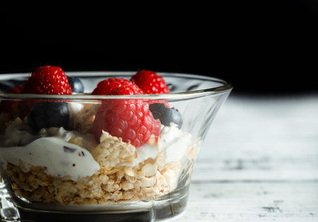 Raspberries, blueberries, cereals and yogurt in a glass bowl on wooden slats. Healthy breakfast for...