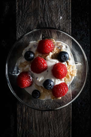 Raspberries, blueberries, cereals and yogurt in a glass bowl on old wooden boards. Healthy breakfast for a healthy life. Vertical image view from above.の写真素材