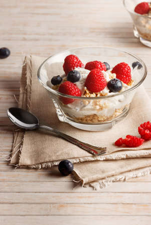 Raspberries, blueberries, cereals and yogurt in a glass bowl on sackcloth and wooden slats. Healthy breakfast for a healthy life. Vertical image.の写真素材