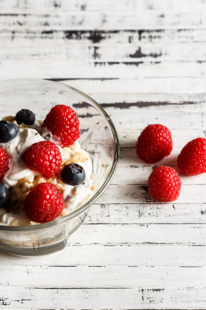 Raspberries, blueberries, cereals and yogurt in a glass bowl on wooden slats. Healthy breakfast for...