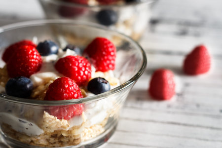 Raspberries, blueberries, cereals and yogurt in a glass bowl on wooden slats. Healthy breakfast for...