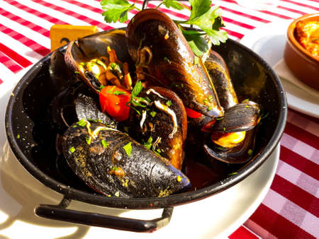 Marinated mussels in a black metal bowl on red and white striped tablecloth. Horizontal image.の素材