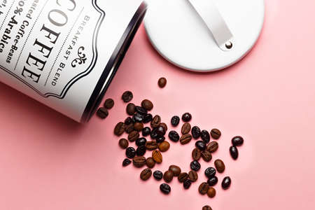 Coffee beans out of coffee pot with pot lid next to it on pink background.の写真素材