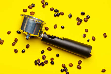 Espresso machine filter holder surrounded by coffee beans on yellow background.の写真素材