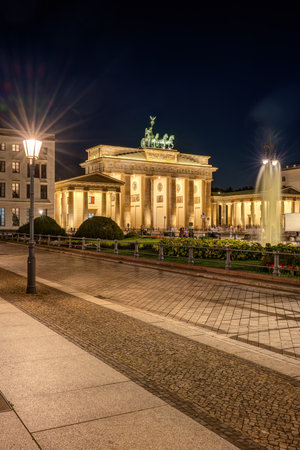 The illuminated Brandenburg Gate in Berlin with a fountain and a street light at nightの写真素材