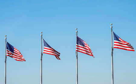 Four US flags waving in the wind against a blue sky