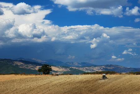 Plowing a field under dark dramatic sky                                