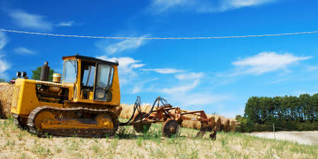 Yellow caterpillar with agricoltural machinery in a fieldの写真素材