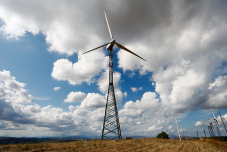 Large trellis wind turbine viewed in dry autumnal field under moody sky