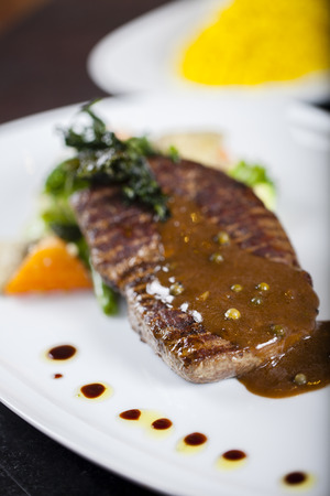 A grilled stake with black pepper sauce, garnished with sautéed green bean and carrotの写真素材