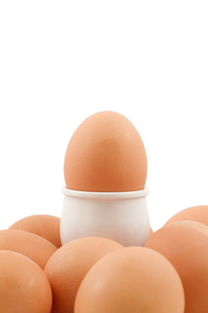 A brown egg in an eggcup surrounded by lots more eggs isolated on white.