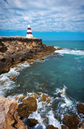 Red and white striped beacon on a cliffs edge overlooking the ocean at the coast.の写真素材