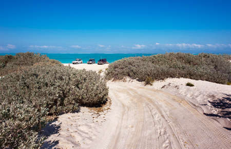 A 4WD track over sand dunes leads down to the beach and the tropical blue sea.の写真素材