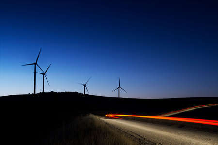 Wind turbines at dusk with car lightsの写真素材