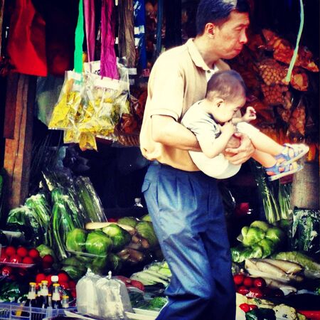 A Man with his child walking in front of vegetable stall in Kundasangの素材