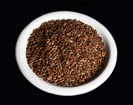 Bowl full of brown flax seed or linseed, on black backgroundの写真素材