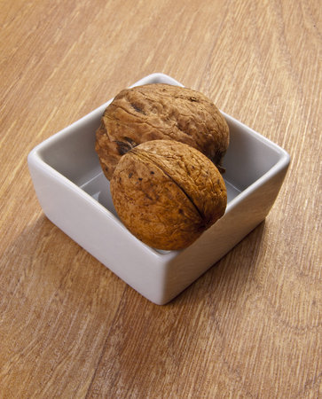 White ceramic bowl with healthy walnuts isolated on wooden background