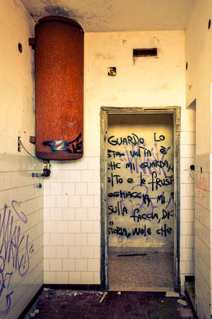 Remains of bathroom in ruins. Rusty water heater and doorway that reveals writing on the wall. Interior of an abandoned building in ruins. Monte Grappa, Vicenza, Italyのeditorial素材