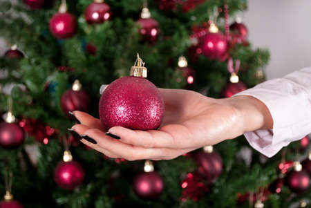 Female hand holding decoration for Christmas tree and blurry tree in background. Close upの写真素材