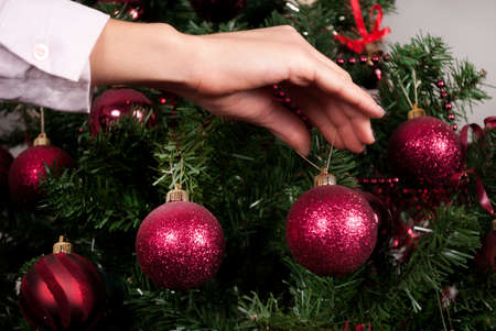 Women hand hang red decoration for Christmas tree and blurry tree in background. Close upの写真素材