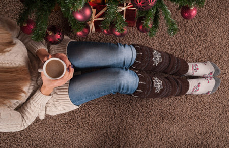 Young girl legs with warmers on floor on carpet with cup of coffee in hand and next to Christmas...