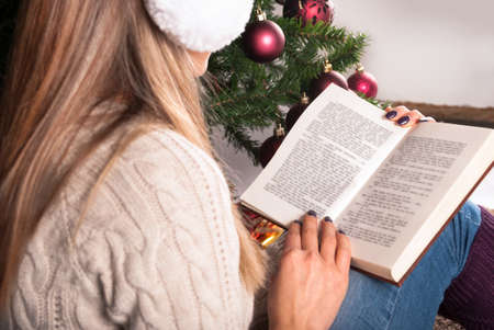 Young girl reading book and sitting on Christmas tree is background, close upの写真素材