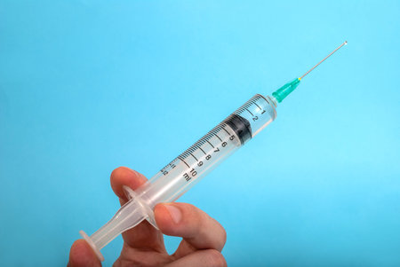 Injection with a needle in the hand and a drop of a drug isolated on a blue background, medical...