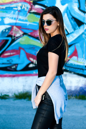 Young girl poses in a beautiful spring day in front of graffiti on the wall in background