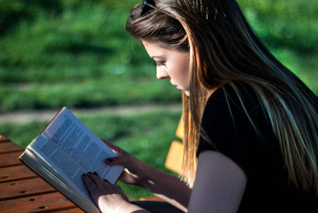 Girl reading a book on sunny spring day in the park on a bench