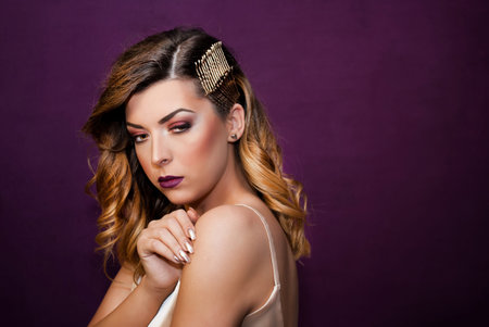 Portrait of beautiful girl with golden curly hair posing on purple wall