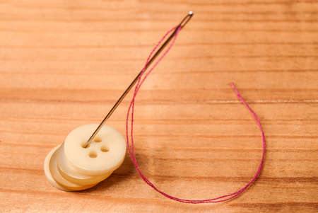 Cloth buttons and sewing needle with thread on wooden deskの写真素材