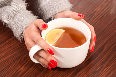 Girl hands holding a cup of tea with lemon on  wooden deskの写真素材