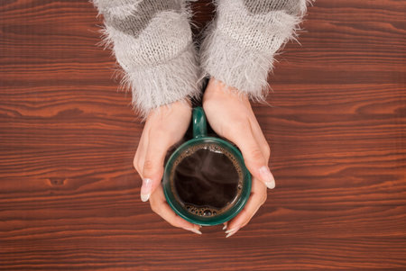 Woman hands holding a cup of coffee on  wooden desk