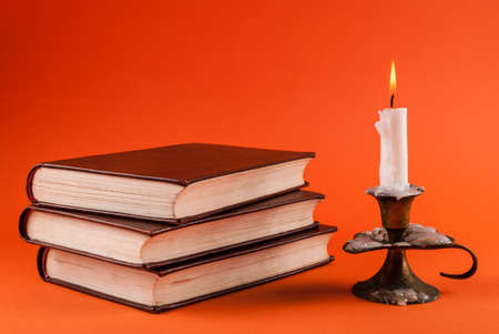 Candle burning in candlestick and three old books isolated on orange backgroundの写真素材