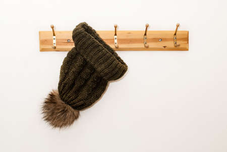 Winter wool cap with a furry ball in green color hanging on a hat stand on white backgroundの写真素材