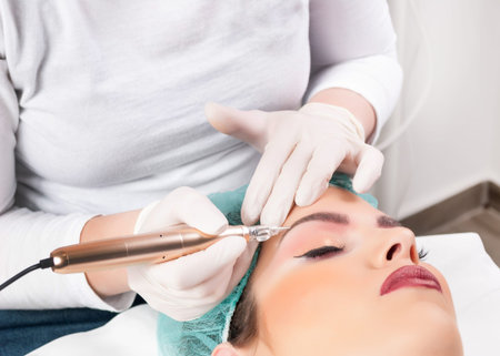 Cosmetologist applying permanent make up on eyebrows in  beauty studio. Eyebrows tattoo