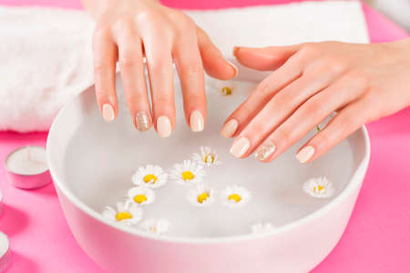 Young girl hands with manicure nails and bowl with water and daisy flower. Manicure and beauty hand concept. Selective focusの写真素材